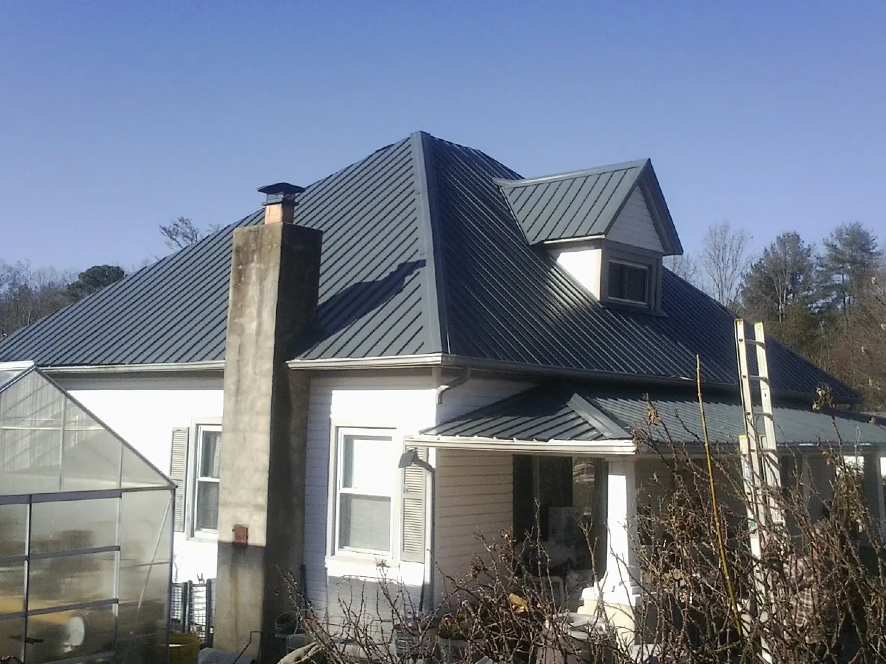 Dark blue standing seam metal roof on a white farmhouse with dormer — Slate & Tile Roof Repair by Roofing Brothers in River Ranch