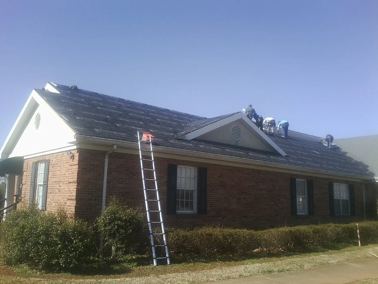 Crew tearing shingles off a brick ranch roof with a ladder set — Metal Roof Repair work by our crew in River Ranch