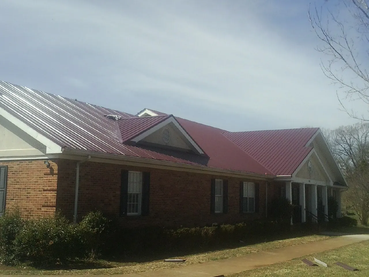 Red metal roof with gabled entries on a long brick building, from a Hail Damage Roof Repair job in River Ranch