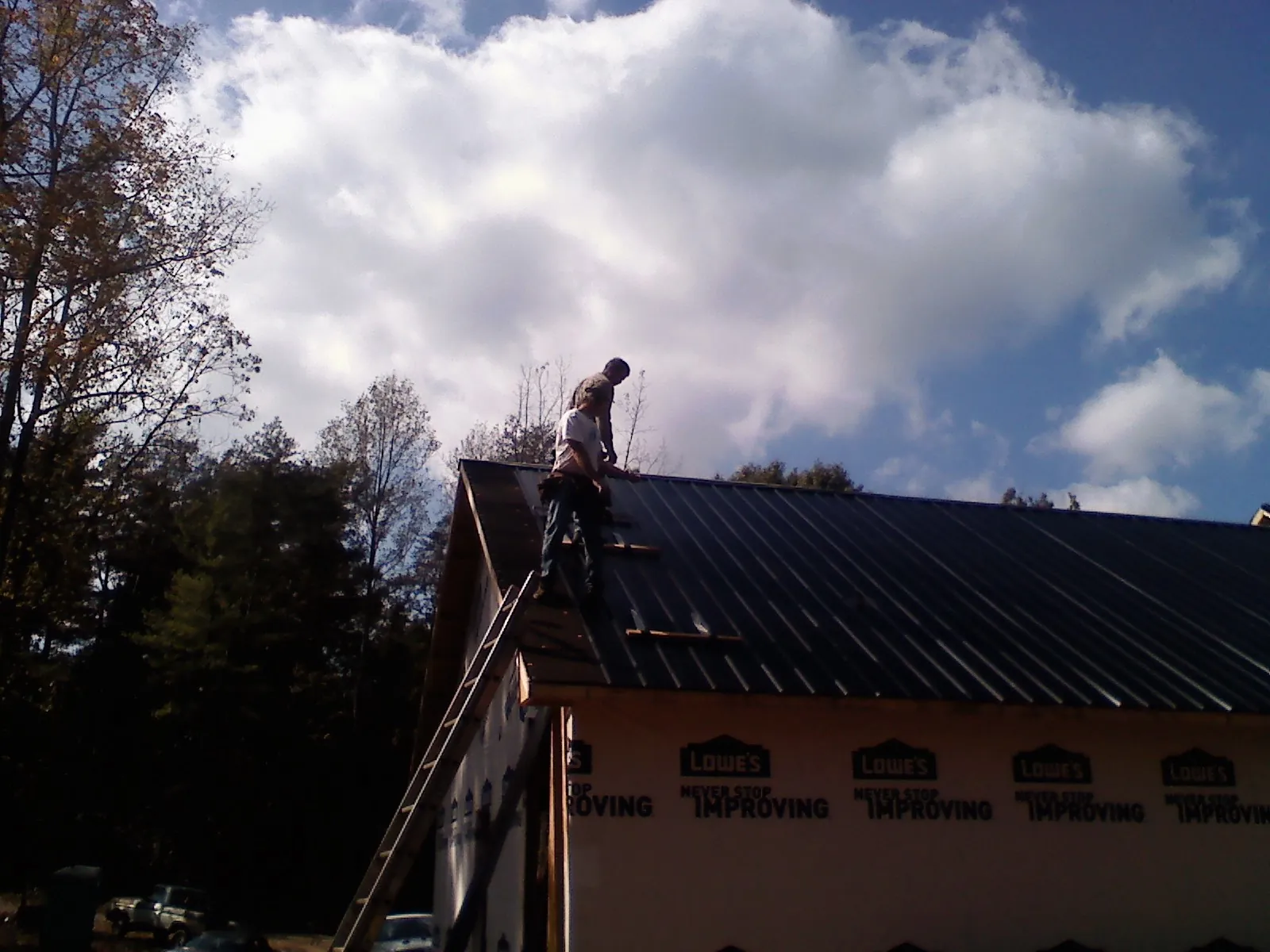 Roofer fastening dark metal panels high against a cloudy sky, from a Roof Inspection job in River Ranch